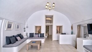 Una sala de estar moderna con una pared blanca curva, un conjunto de sofás, una mesa de centro y un televisor.