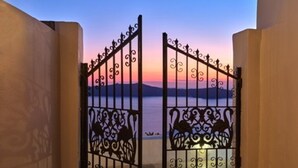 Una entrada protegida con intrincados trabajos de metal que da a una vista de un cuerpo de agua y montañas distantes al atardecer.