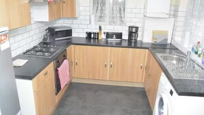 A kitchen with wooden cabinets, a gas stove, a microwave, a toaster, and a washing machine. - 4 Bedroom House in Grays - Sleeps 6 & Parking (Grays)