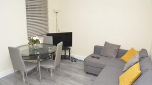 A modern living room with a glass dining table, grey sofa, and a TV. - 4 Bedroom House in Grays - Sleeps 6 & Parking (Grays)