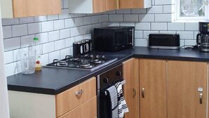 A kitchen with a gas stove, microwave, and toaster. There is a window with a view of trees. - 4 Bedroom House in Grays - Sleeps 6 & Parking (Grays)