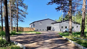 Un chalet avec une allée en gravier, entouré d’arbres et délimité par une clôture en bois.