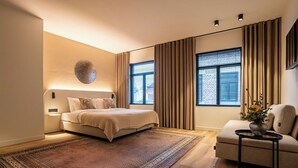 Un dormitorio moderno con una cama grande, una zona de estar con sofá y un elemento decorativo en la pared.