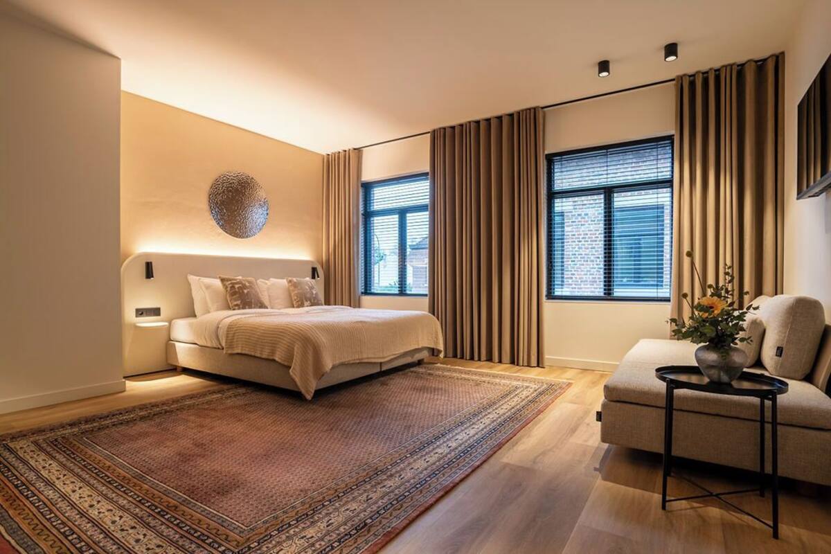 A modern bedroom with a large bed, a sitting area with a sofa, and a decorative wall piece.