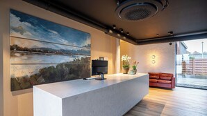 Un área de recepción moderna con un cuadro grande, un mostrador de recepción, un televisor de pantalla plana y un sofá de cuero rojo.