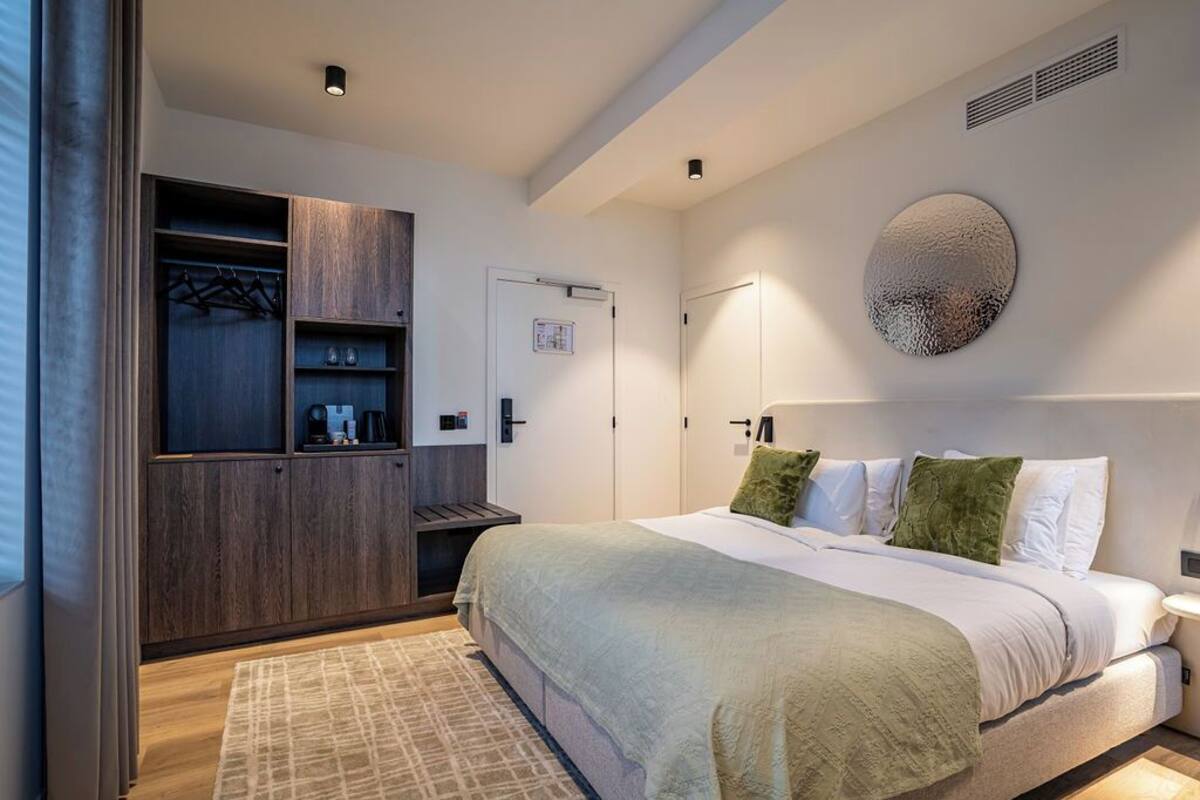 A modern bedroom with a large bed, a wardrobe, and a wall-mounted artwork.