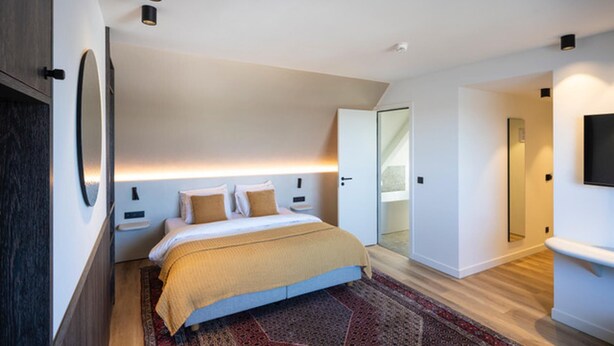 A modern hotel room with a large bed, a bedside table, a mirror, and a TV. - Boutique Hotel Annamaes (Lanaken)