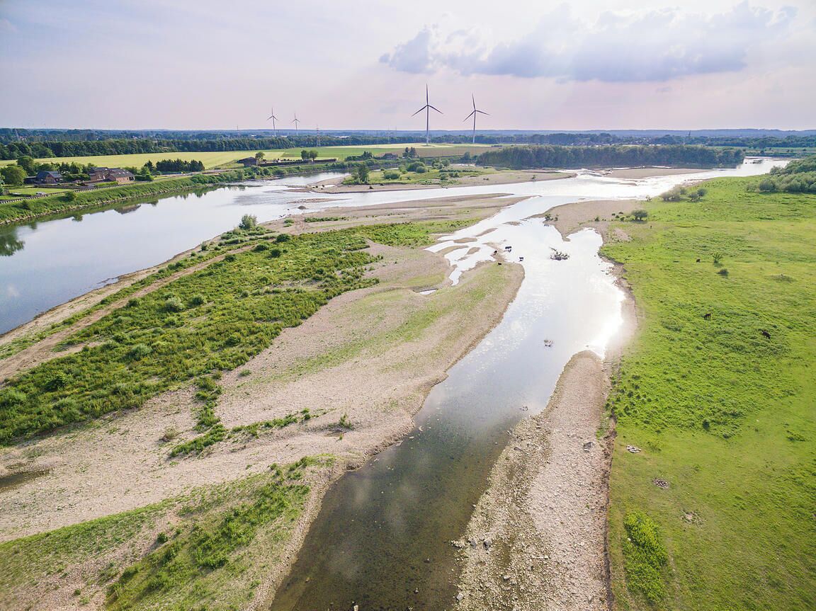 Een rivier slingert door een landelijk gebied, met windmolens in de verte.