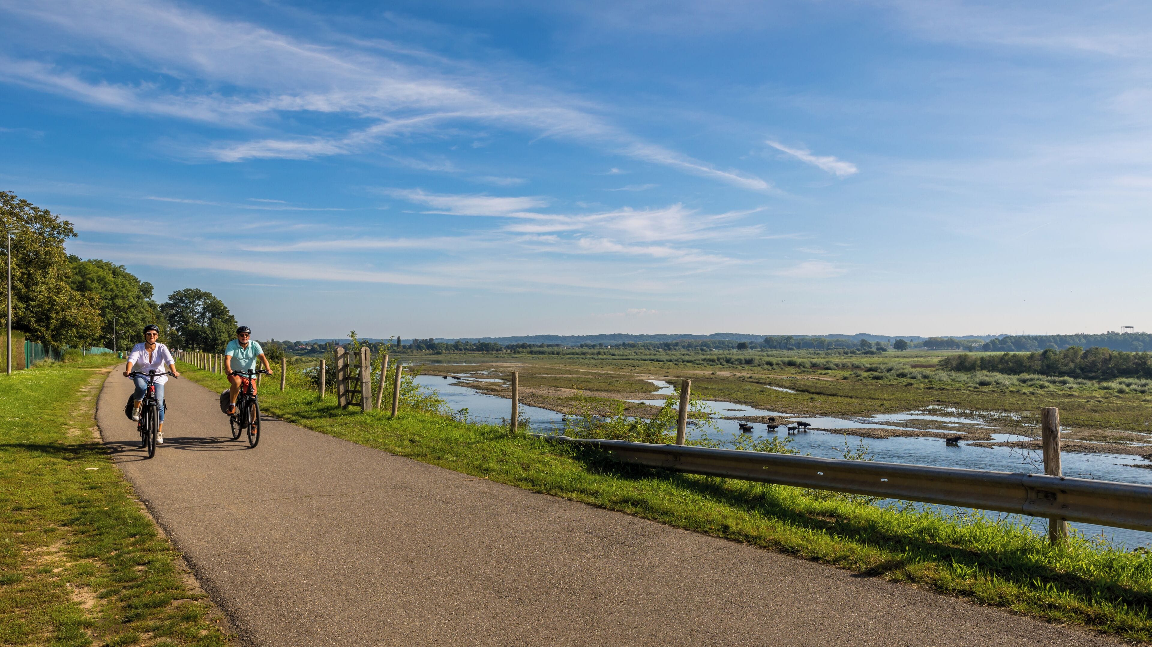 A paved path alongside a river with a wooden fence and a metal railing.