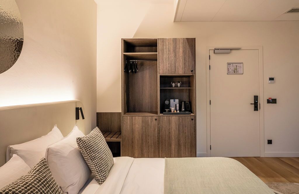 Un dormitorio con cama, armario de madera, puerta y lámpara fijada a la pared.