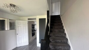 A staircase leading to a second-floor landing with a modern kitchen and a door to another room. - Housesleeps6-freeparking-wifi-contractors-garden (Billingham)