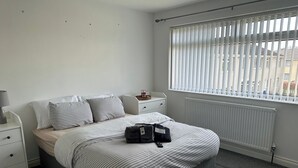 A bedroom with a bed, a nightstand, a lamp, a radiator, and a window with blinds. - Housesleeps6-freeparking-wifi-contractors-garden (Billingham)