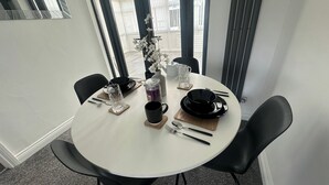 A round dining table with black chairs, a vase with white flowers, and various dining utensils. - Housesleeps6-freeparking-wifi-contractors-garden (Billingham)