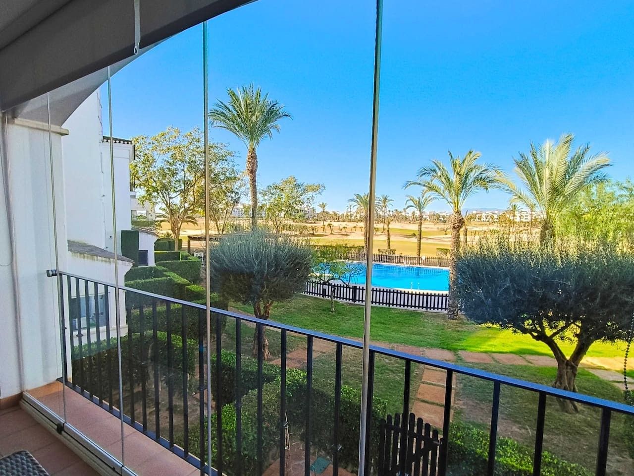 A balcony with a view of a swimming pool, palm trees, and a well-maintained lawn.
