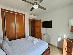 Ein Schlafzimmer mit Bett, Deckenventilator, Klimaanlage, Fernseher und einem Schminktisch.