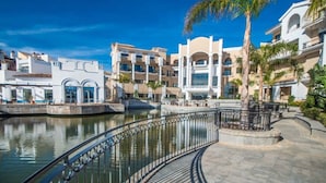 Un hotel frente al agua con un paseo curvo, palmeras y una piscina.