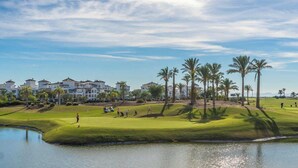 A golf course with a pond, palm trees, and buildings in the background. - Bright Apartment with Stunning Swimming Pool Views - MO4812LT (Torre-Pacheco)