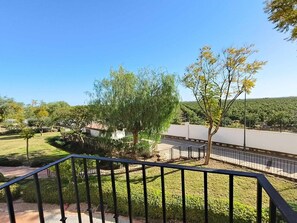 Ein Balkon mit Blick auf einen angelegten Garten, ein weißes Gebäude und eine Straße.