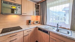 Cozinha compacta com armários de madeira, micro-ondas embutido, torradeira e janela com cortinas.
