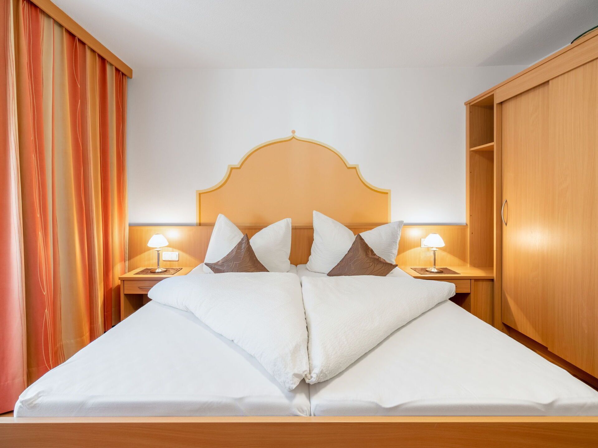 Ein Hotelzimmer mit einem hölzernen Bett, zwei Nachttischen mit Lampen und einem Kleiderschrank.