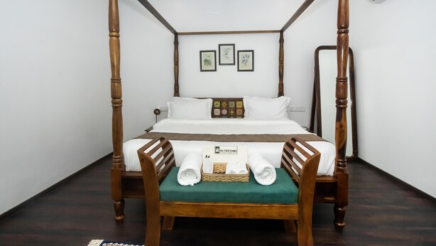 A four-poster bed with a wooden frame, a green upholstered bench, and a set of towels on the bench. - The Tiger Claws Tadoba (Chimur)