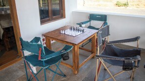 A wooden table with a chessboard, two green folding chairs, and a black folding chair. - The Tiger Claws Tadoba (Chimur)