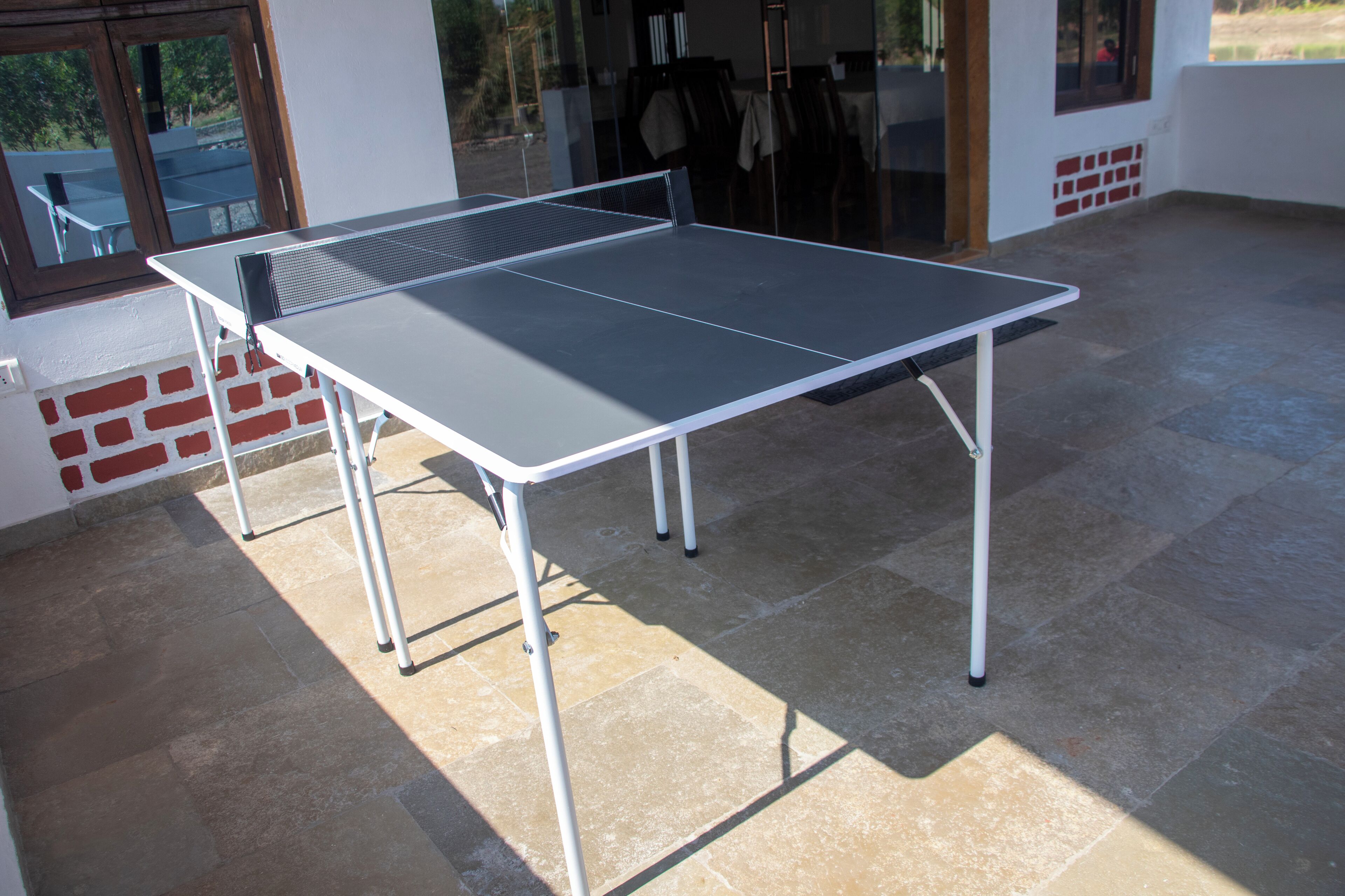 A ping pong table in an outdoor area with a tiled floor and a brick wall.