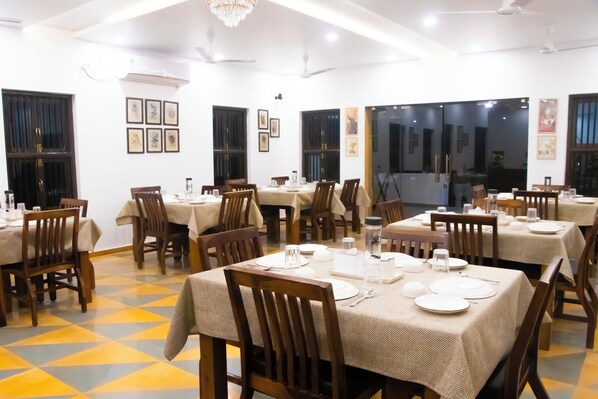 A dining area with multiple tables set for meals, featuring wooden chairs and tables covered with beige tablecloths. - The Tiger Claws Tadoba (Chimur)