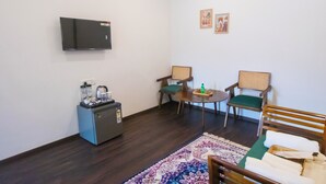 A compact room with a flat-screen TV, a small kitchenette, two chairs, a round table, and a patterned rug. - The Tiger Claws Tadoba (Chimur)