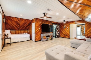 A spacious room with a bed, a sofa, a TV, and a ceiling fan.