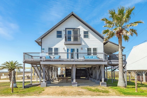 A two-story house with a balcony, a palm tree, and a clear sky.