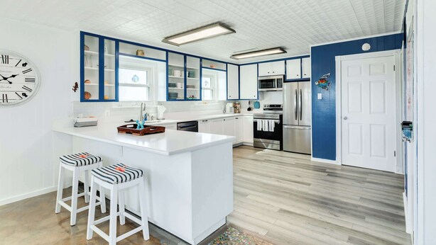 Une cuisine moderne avec des meubles blancs, un îlot central doté de tabourets, une horloge et un four à micro-ondes.