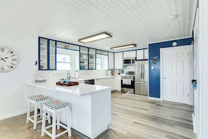 A modern kitchen with white cabinetry, a central island with stools, a clock, and a microwave.