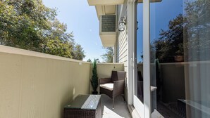 A balcony with wicker furniture, a potted plant, and a glass door leading to an outdoor area.