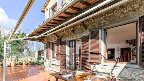 A stone building with wooden shutters, a wooden deck, and a dining table set for four. - Stunning private villa for 8 guests with WIFI, TV, patio and pets allowed (Montieri)