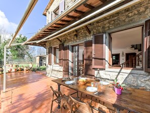 Edifício de pedra com venezianas de madeira, um deck de madeira e uma mesa de jantar posta para quatro pessoas.