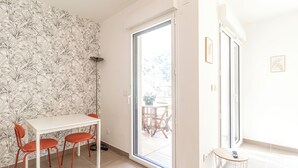 A room with a white table and red chairs, a patterned wallpaper, and a sliding glass door leading to an outdoor area with a table and chairs.