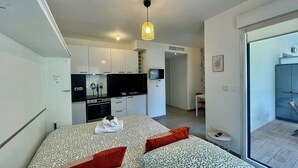 A modern bedroom with a patterned bedspread, a flat-screen TV, a kitchenette, and a sliding glass door to the outside.