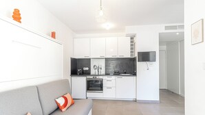 A modern kitchen with white cabinets, a built-in oven, and a flat-screen TV.