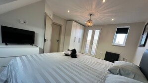 Ein Schlafzimmer mit einem großen Bett, einem Flachbildfernseher, einem Kleiderschrank und einem Fenster mit Jalousien.