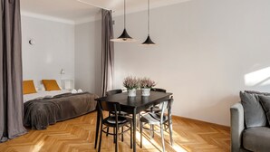 A modern hotel room with a wooden herringbone floor, a bed with a gray headboard, a gray sofa, a dining table with two chairs, and two pendant lights. - ShortStayPoland Piwna B79 (Warsaw)