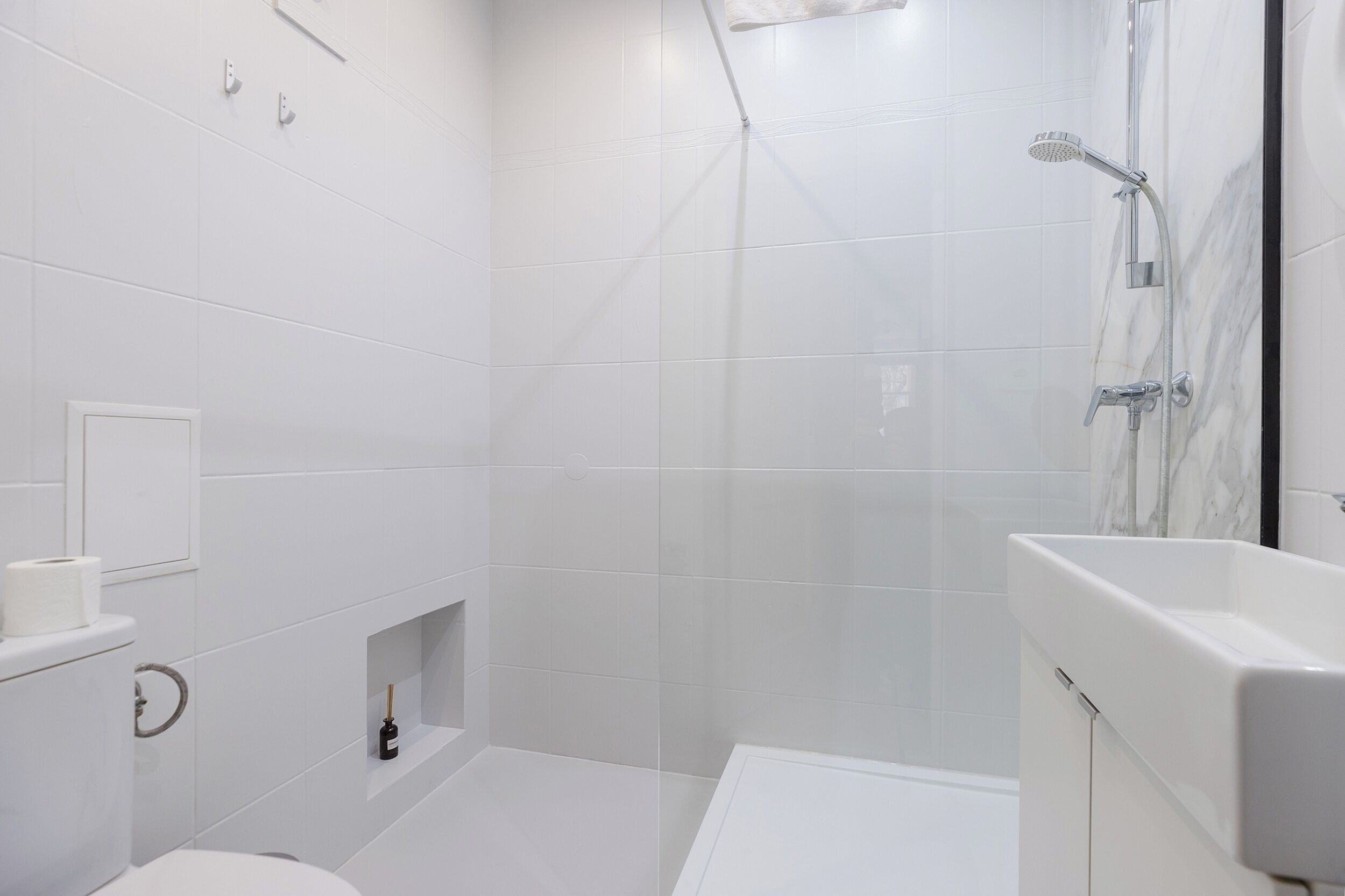 Un baño moderno con azulejos blancos, ducha e inodoro.