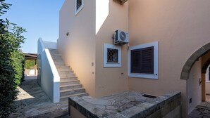 Un edificio de fachada color beige, con una escalera de piedra y un pequeño ventanal con persianas.