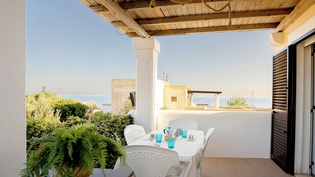 Un área de comedor al aire libre con techo, con una mesa dispuesta para dos personas, que ofrece vistas panorámicas al mar.
