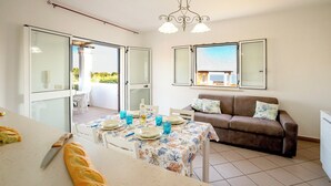 Un área de comedor con una mesa preparada para dos personas, un sofá marrón y vistas al exterior a través de una puerta de vidrio.