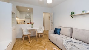 Uma sala de estar moderna com sofá, uma mesa de jantar com cadeiras, uma área de cozinha e um corredor que dá para outro quarto.