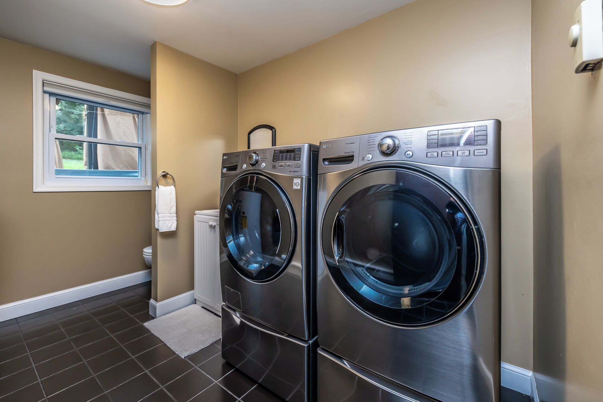 A laundry room with two front-loading washing machines, a window, and a towel rack.