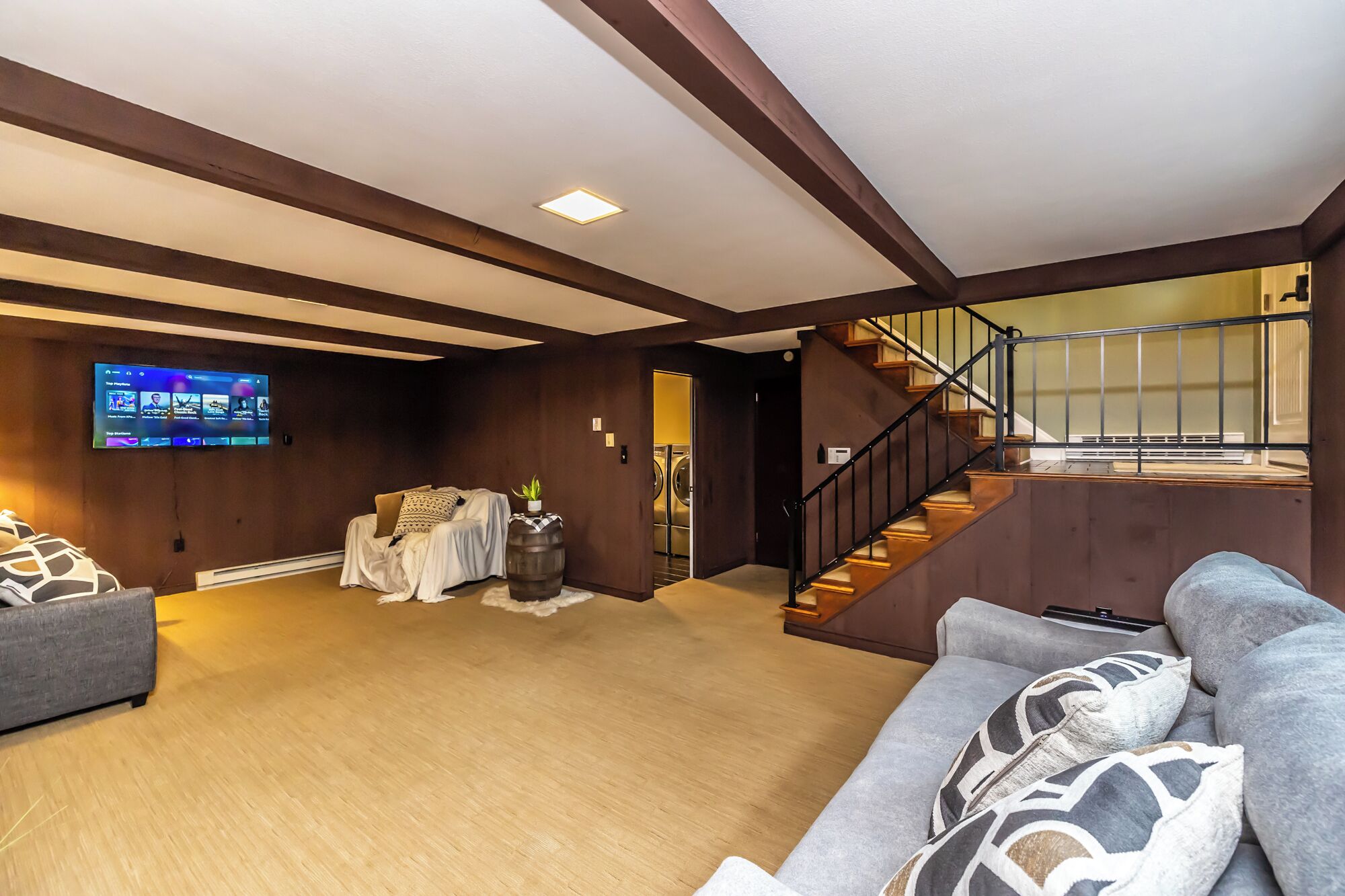 A spacious living room with a large flat-screen TV, a cozy sofa, and a staircase leading to an upper level.