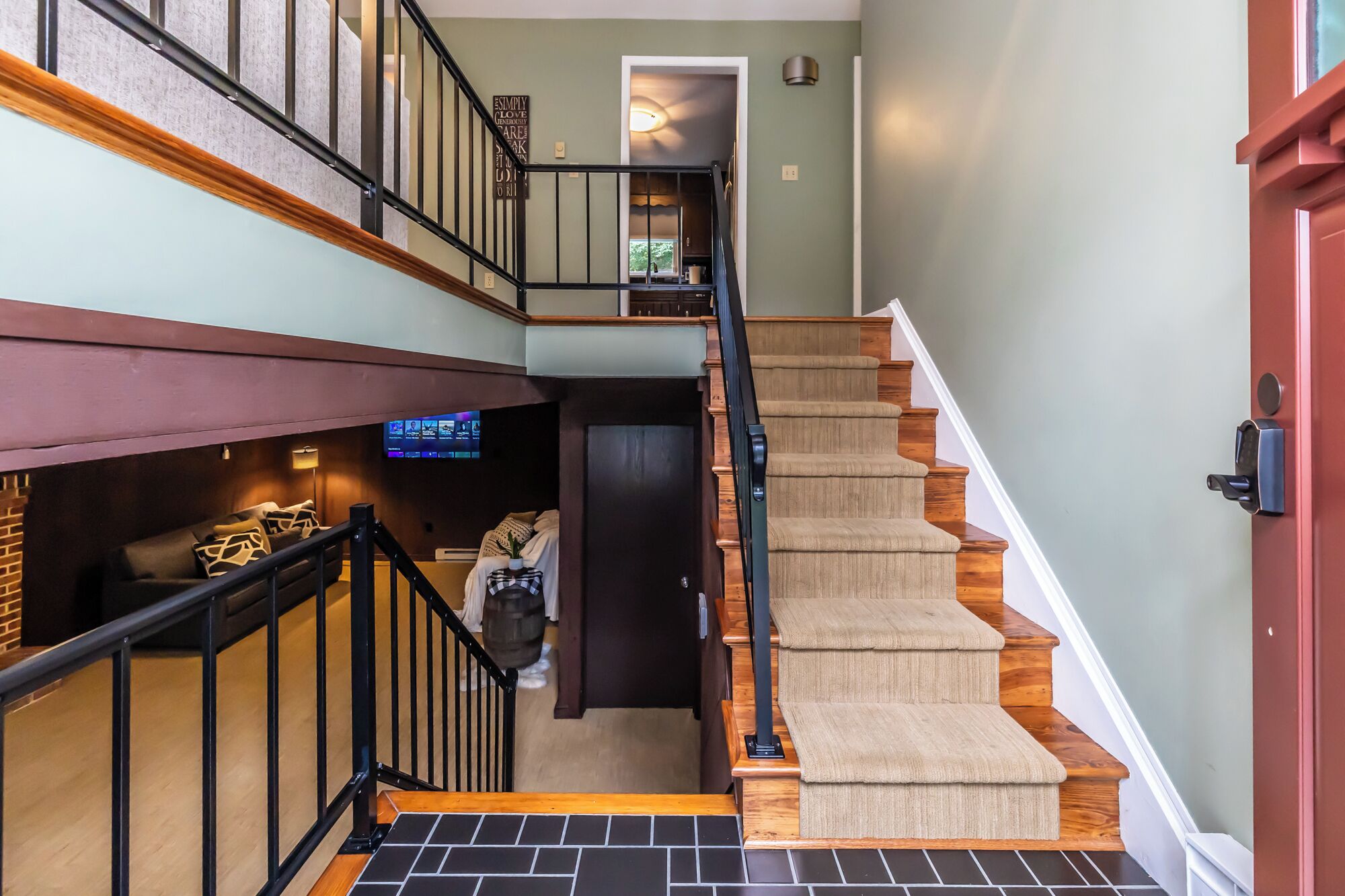 Un intérieur à plusieurs niveaux comprenant un escalier, un téléviseur à écran plat et une porte dotée d’un système de verrouillage à clavier.