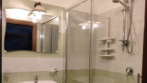Un baño con ducha envuelta en vidrio, lavamanos pedestal y espejo sobre él.